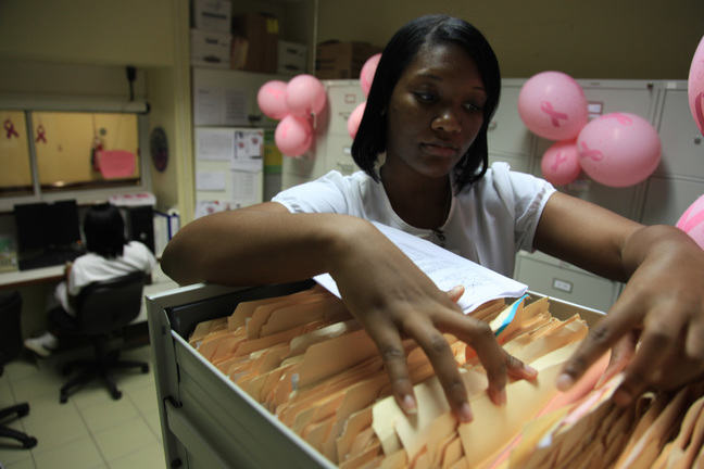 a nurse stands at an open filing cabinet, looking through patient files