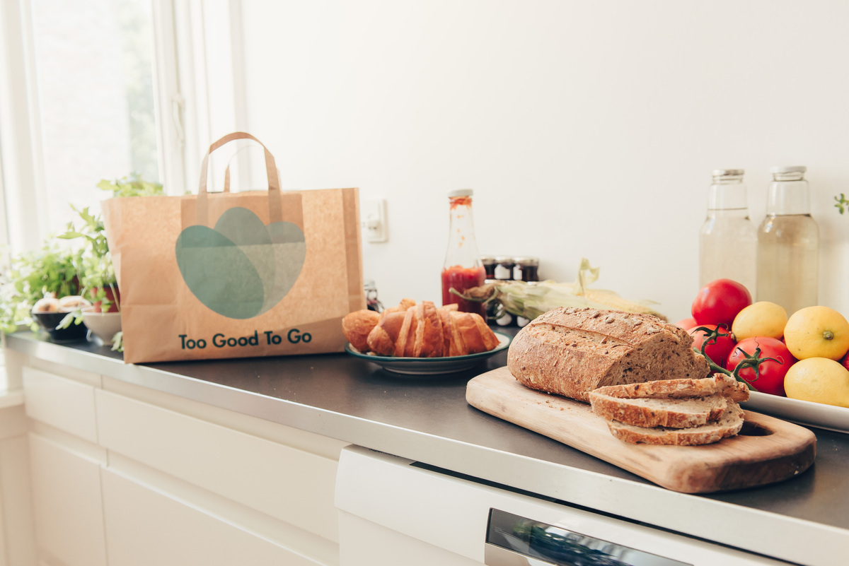 Various food items on a kitchen worktop with a brown paper 'Too Good To Go' bag by the side