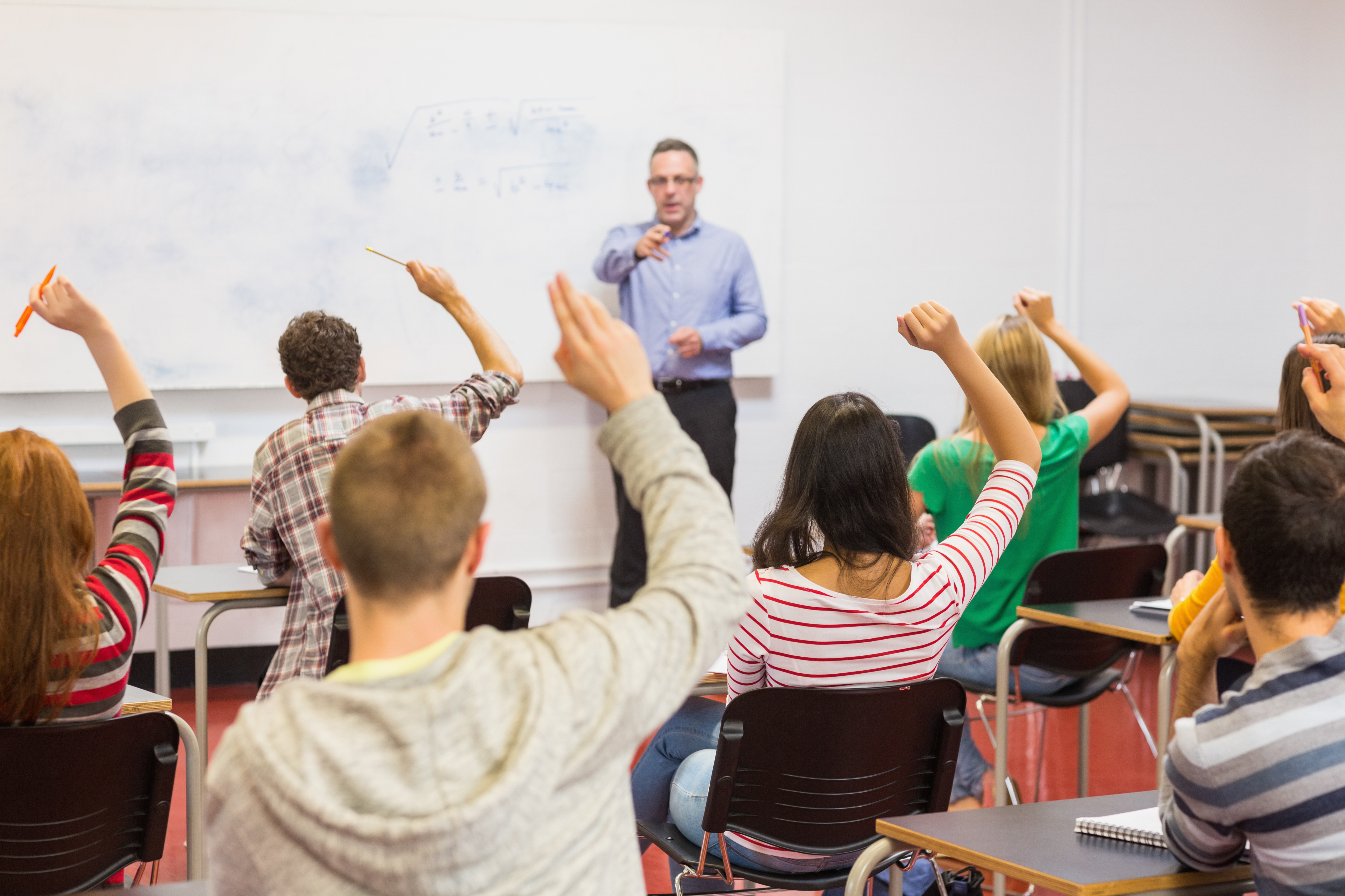 A teacher pointing to a student with their hand raised