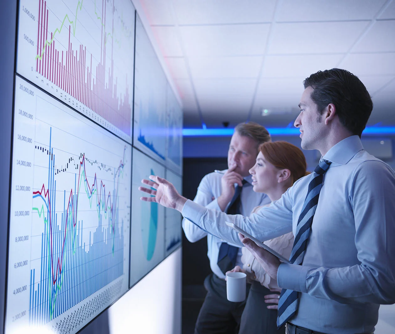 3 business people discussing financial data on a giant screen