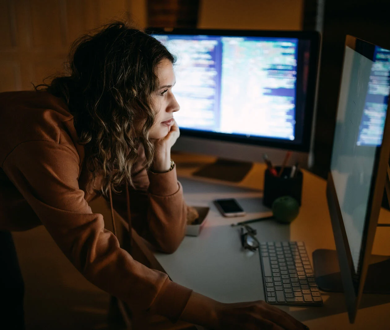 Young IT support woman using 2 monitors computer with coding document in a dark room, doing business in Web3. 