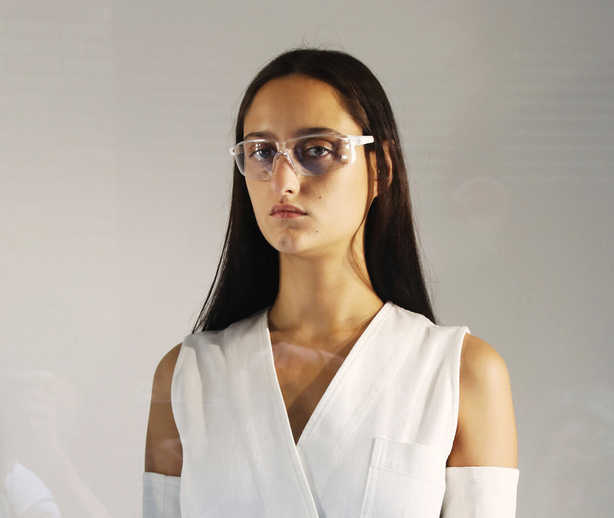 A model posing wearing a white garment and glasses.