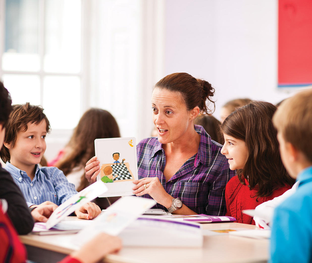 An English language teacher shows a colourful card to a group of young children around her 