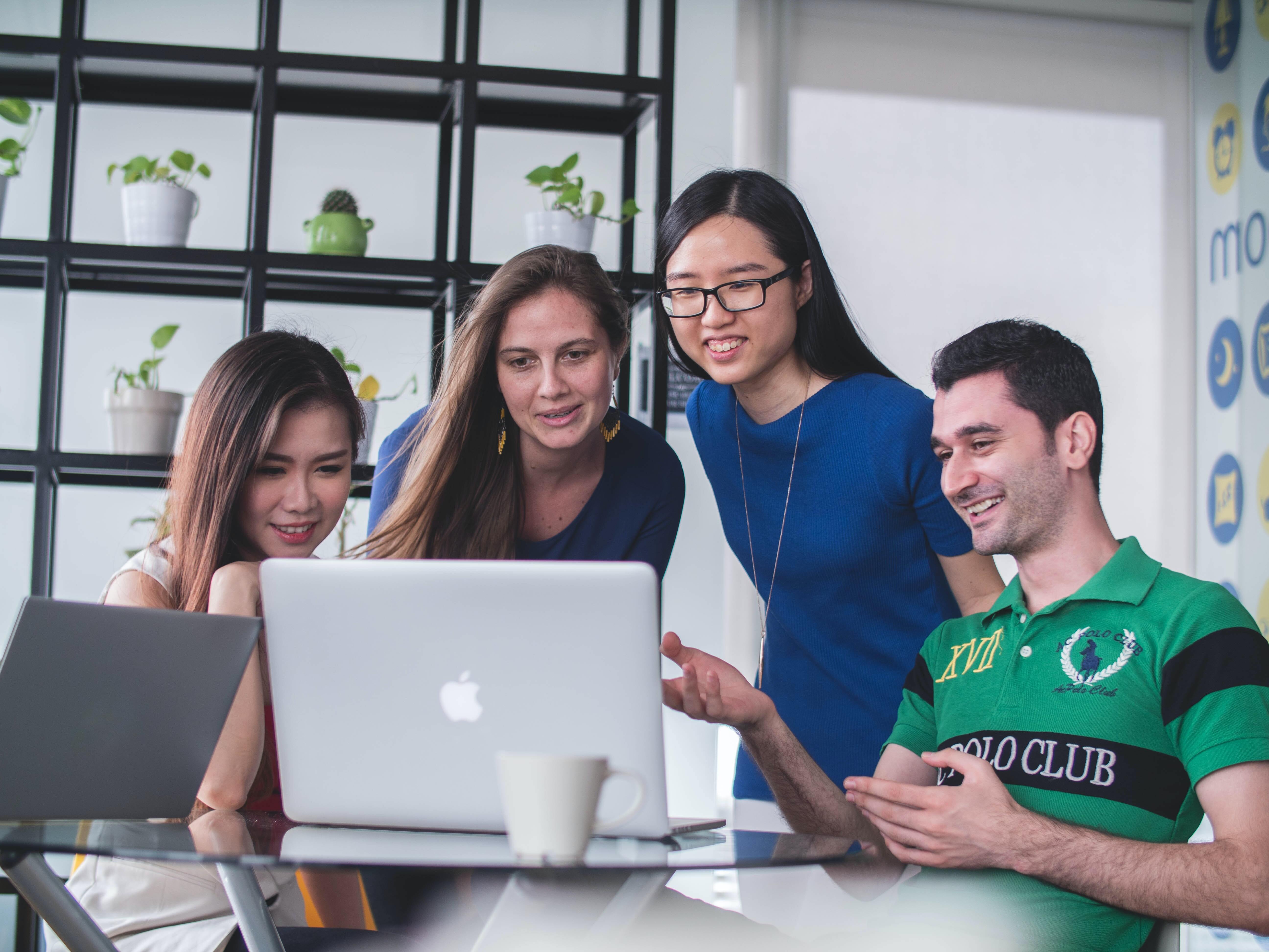 Four people chatting and working around a lap top