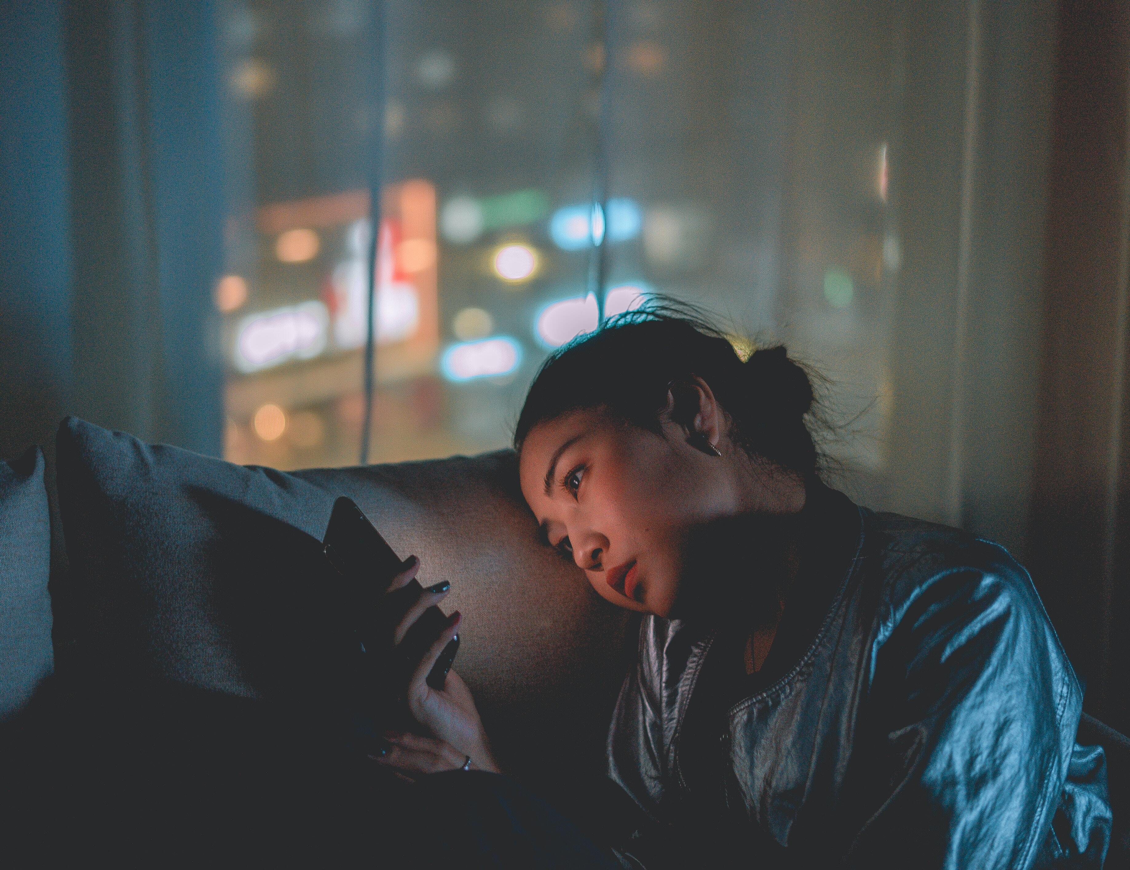 A woman scrolls on her phone in the evening.