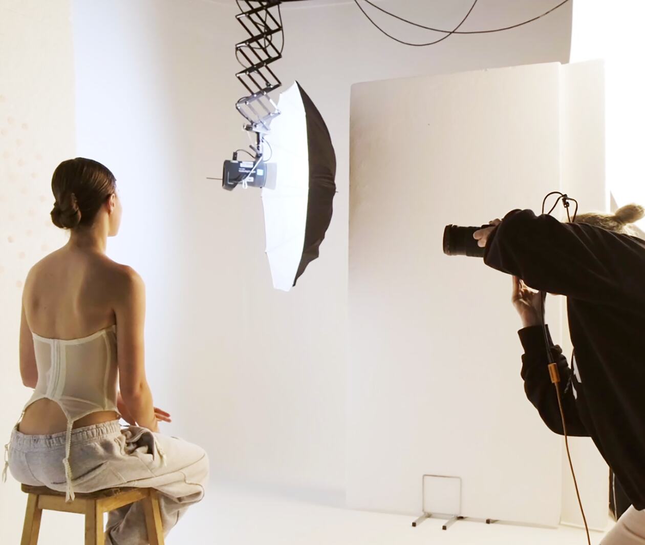 Photographer taking picture of fashion model in studio space with lighting equipment.