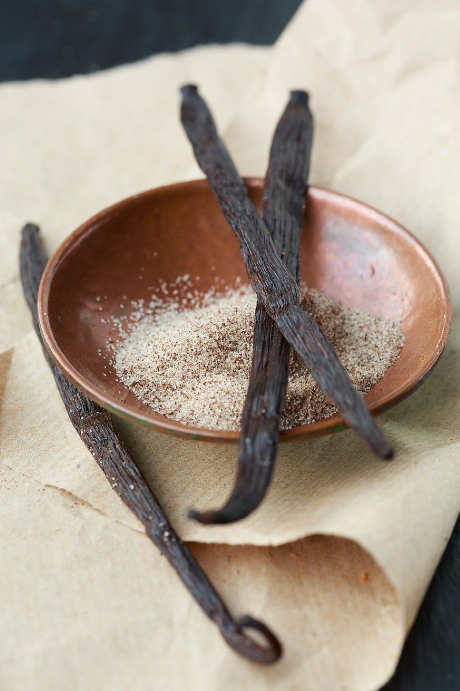 A bowl of sugar with two vanilla pods balanced on top of it and another at the side of it