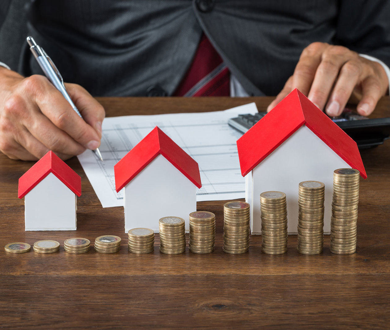 Businessman sits calculating behind set of model houses.