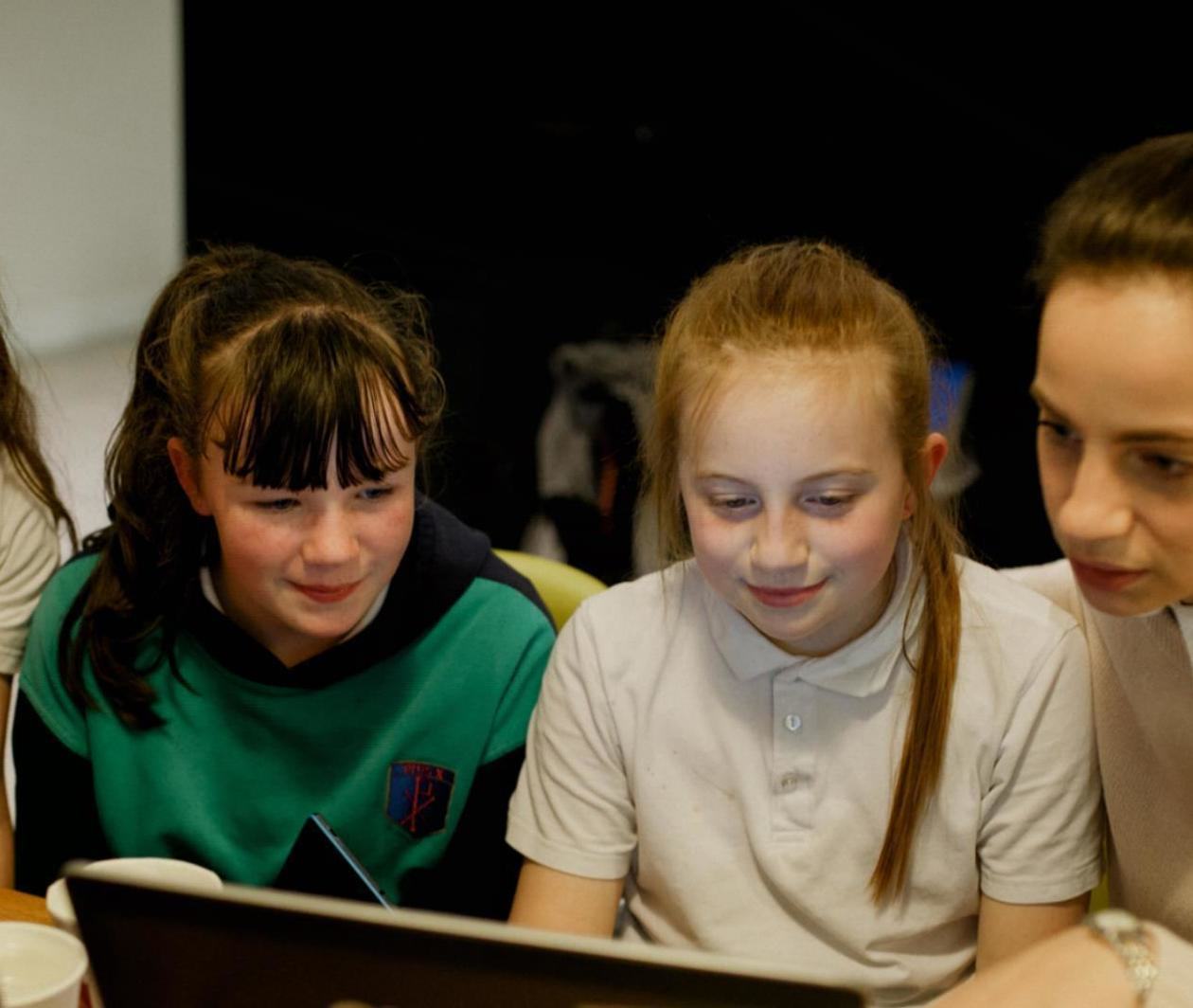 A female teacher and three girls looking at a computer screen