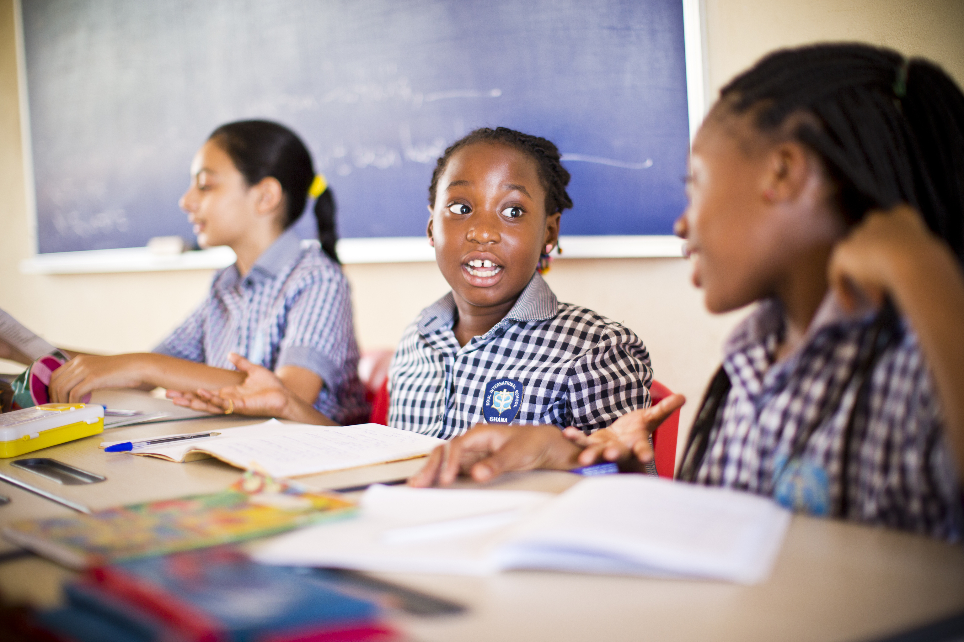 Two young girls talking in a classroom.