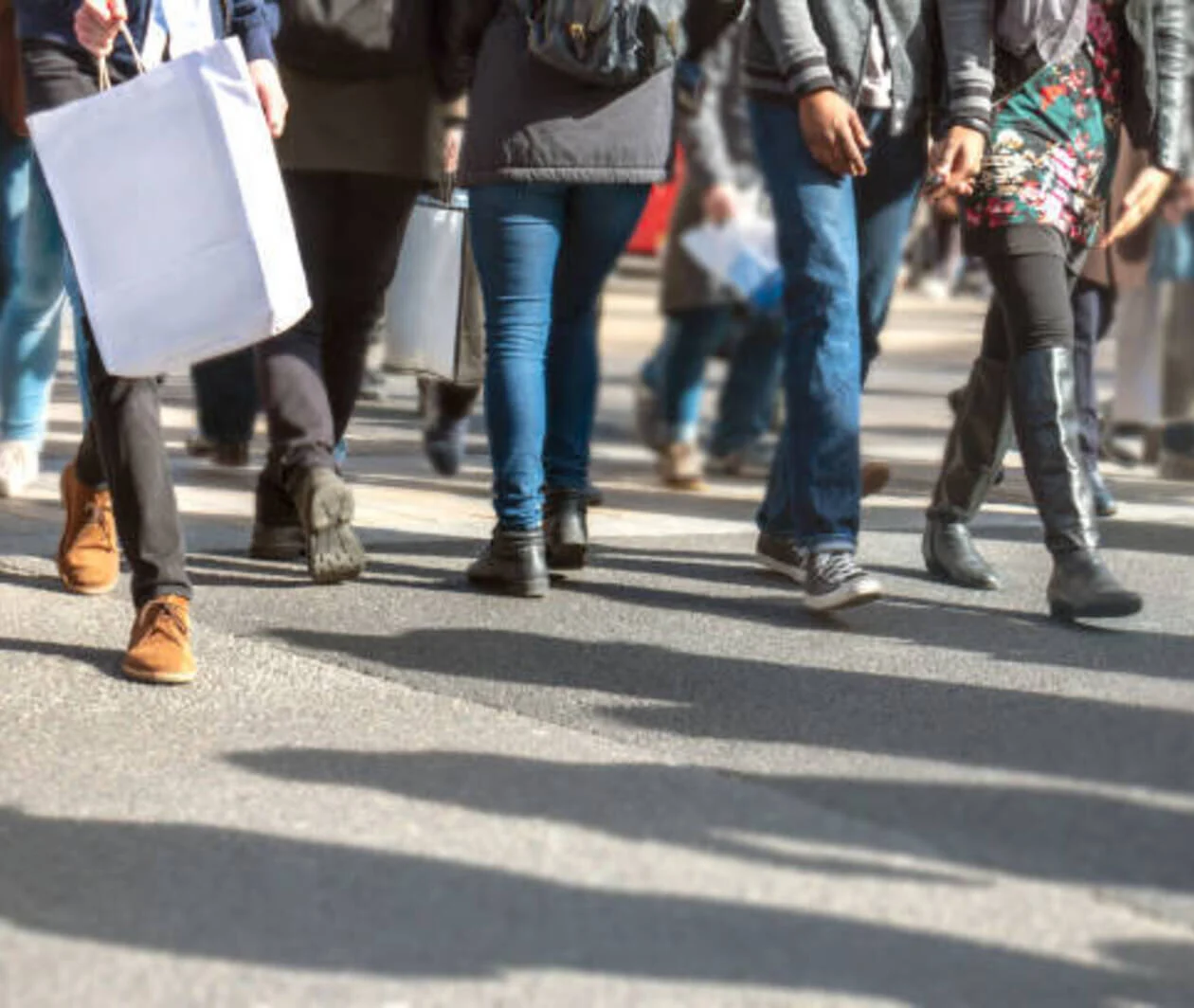 Abstract urban scene of busy city life. The curb is filled with multicultural people crossing while carrying shopping bags. Many punters are buying presents and taking advantage of special discount offers at city retail stores. Shallow focus.