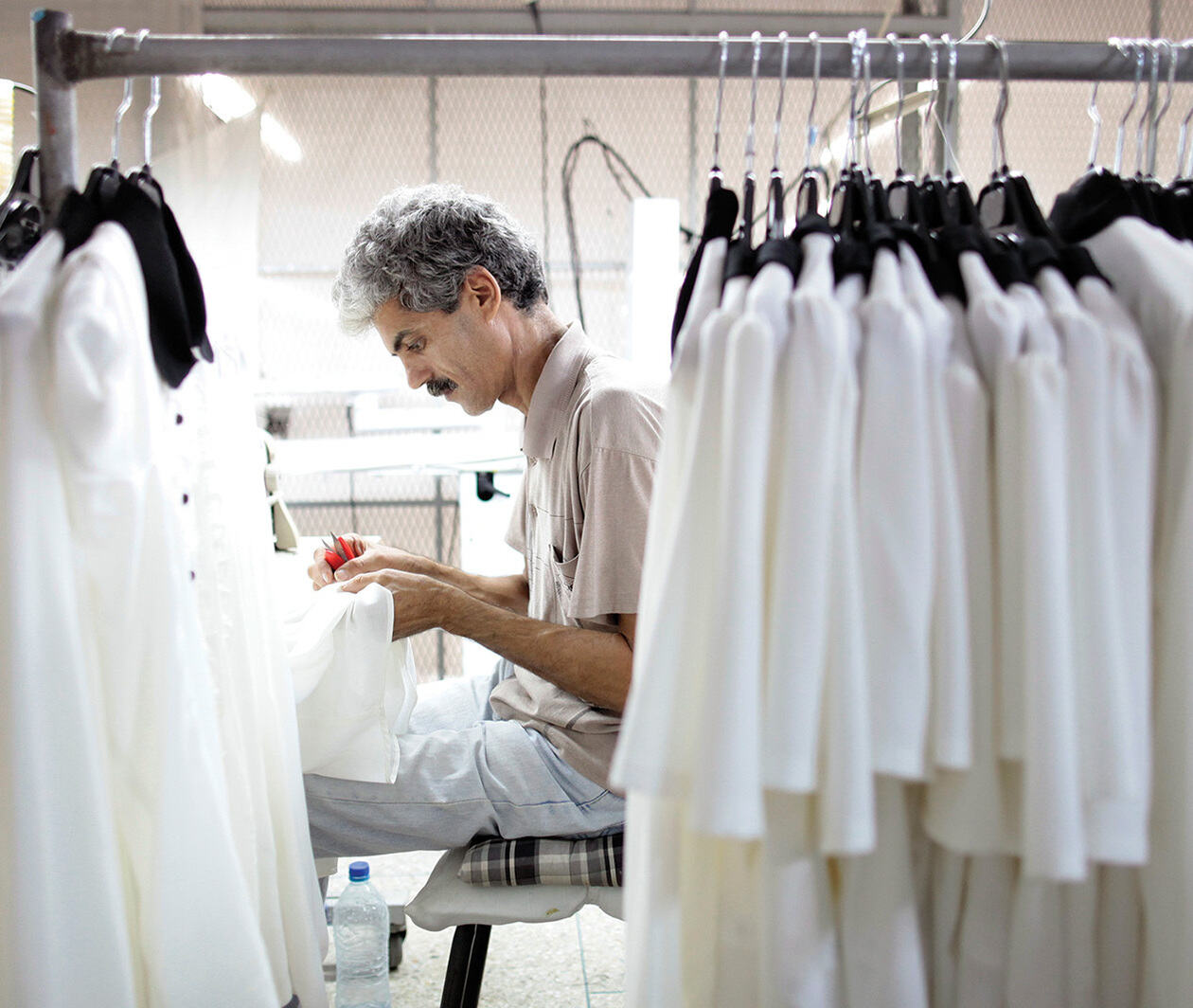 A man working on some textiles with clothes hanging beside him.