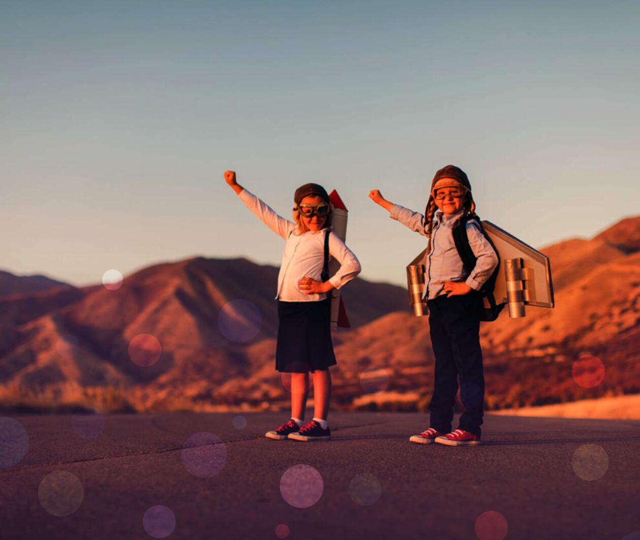 Two little kids with rocket backpacks and goggles, fists raised to the sky.