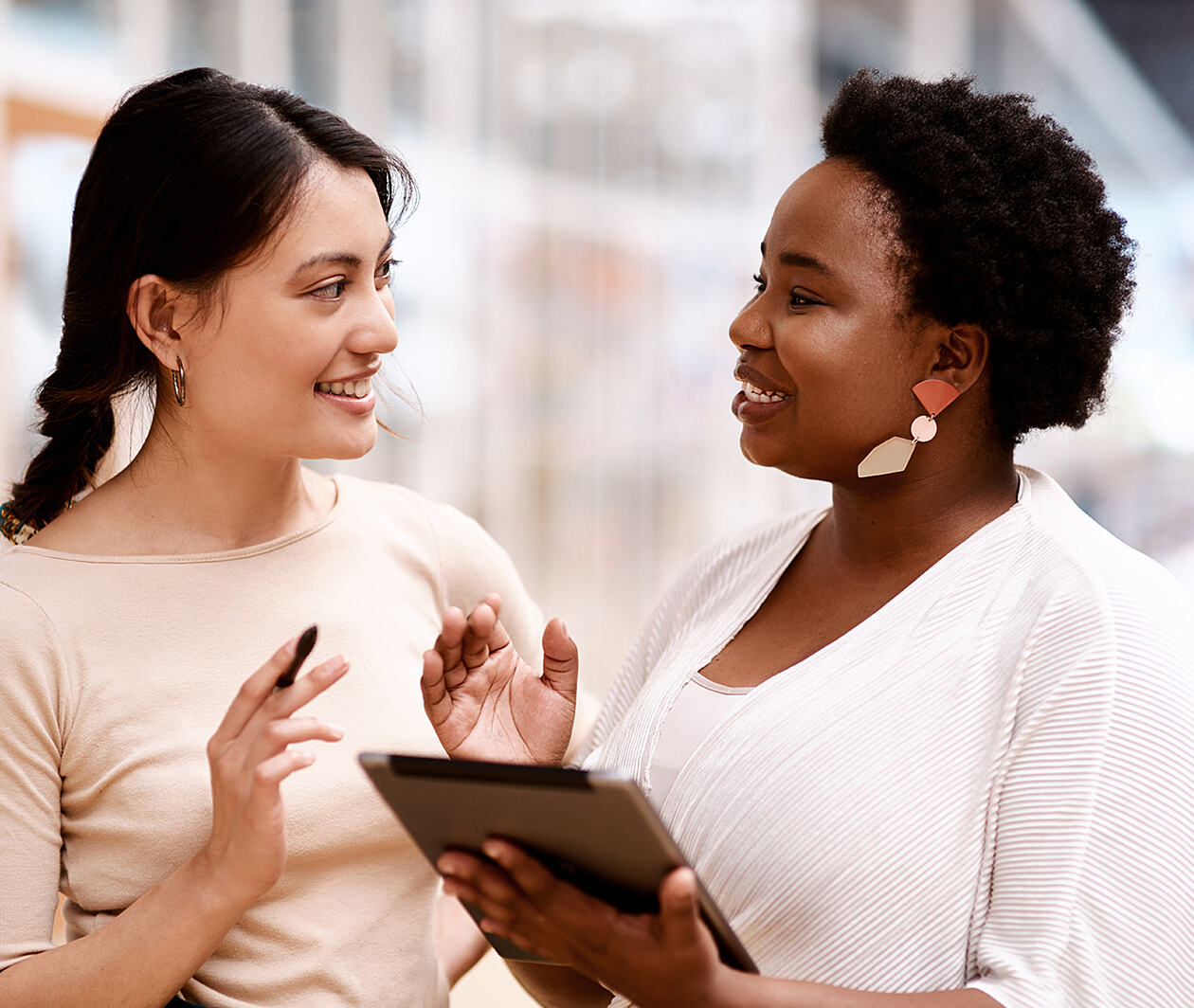 Two women talking and smiling, one is holding a tablet.