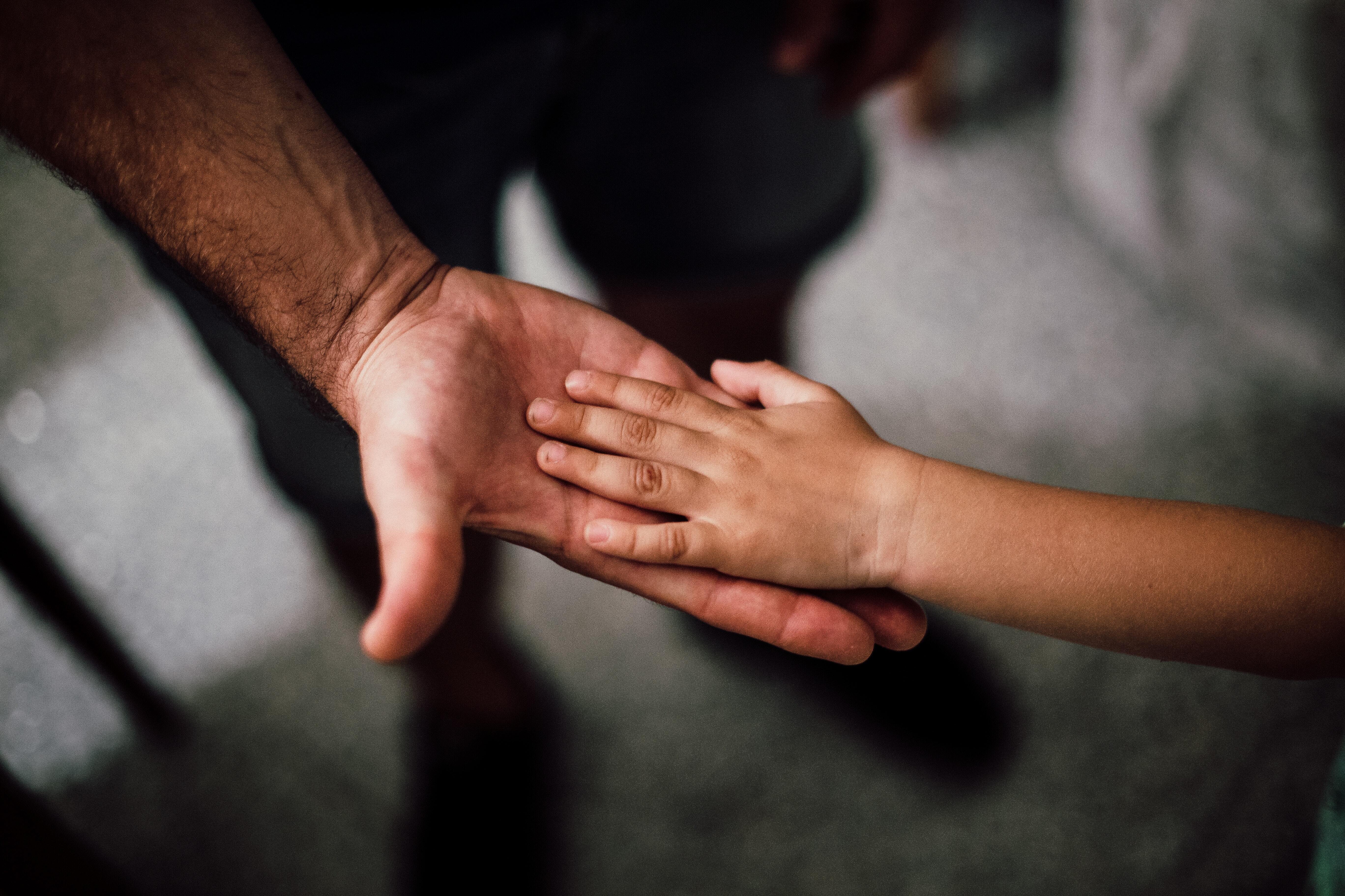 The hand of a child on top of the hand of an adult