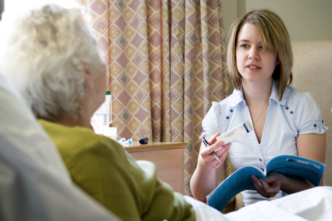 A carer going through some paperwork and medication with a resident at her bedside