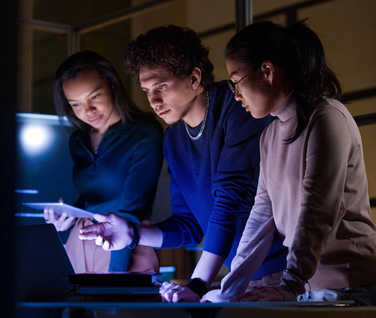 Three students workong on a problem together in a computer in a illuminated room from computer screens