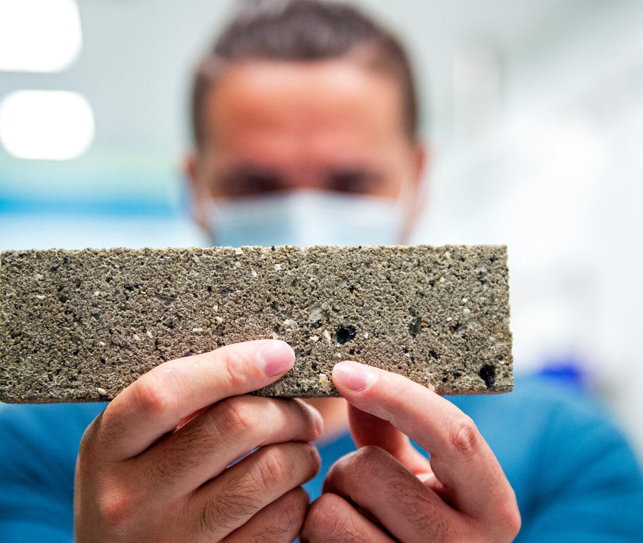 A closeup of a man holding a piece of rectangular sustainable block of concrete.