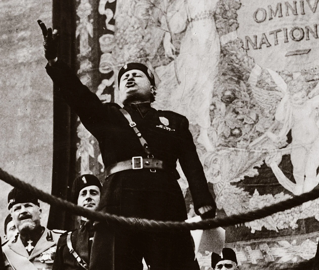 Benito Mussolini on a stage gesturing to an audience