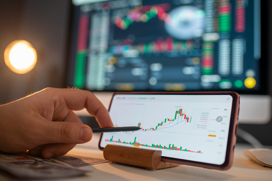 Trader analysing global market price on network diagram on their phone. There's a stock market screen in the background. They are working with the graph and financial reports.