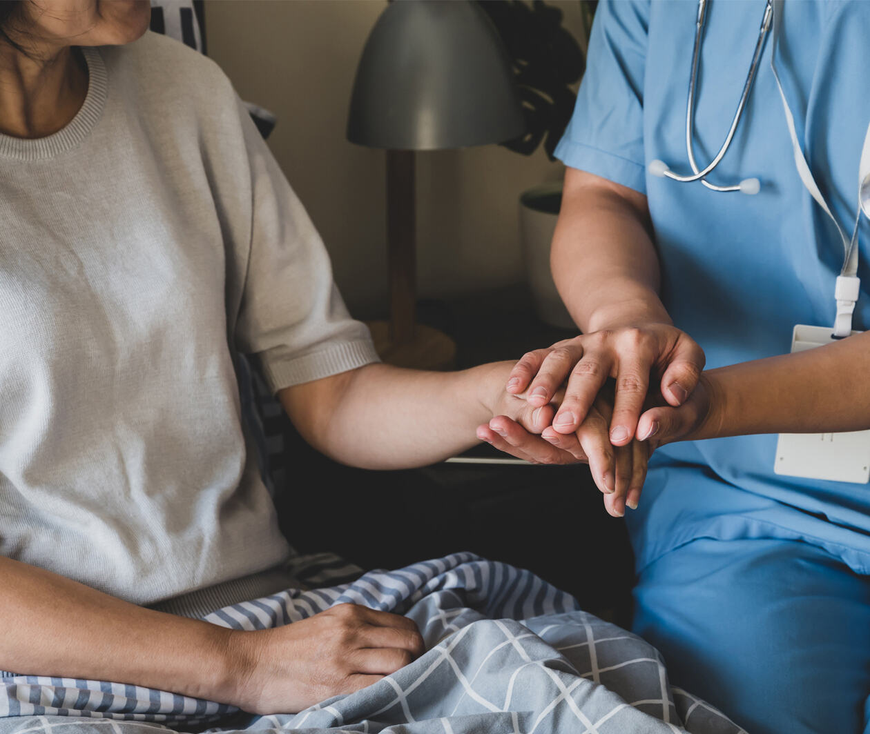 Female home caregiver holding female patient hands to support her speedy recovery from her illness in the bedroom.