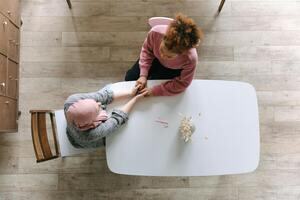 An aerial photo of two woman at a table holding hands.