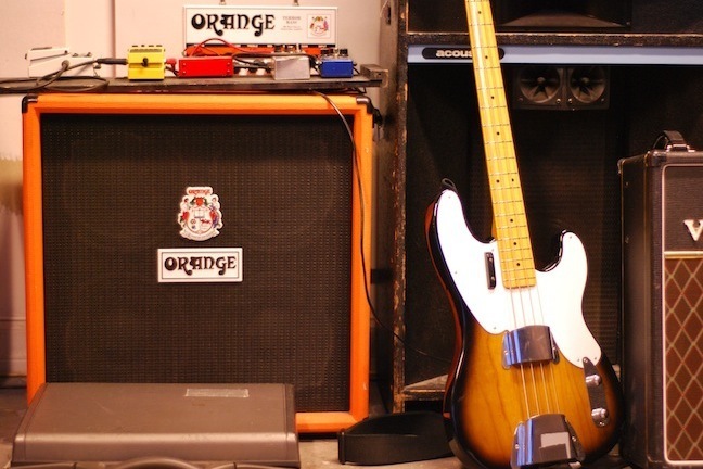 Three amplifiers and a bass guitar against a white colored wall.