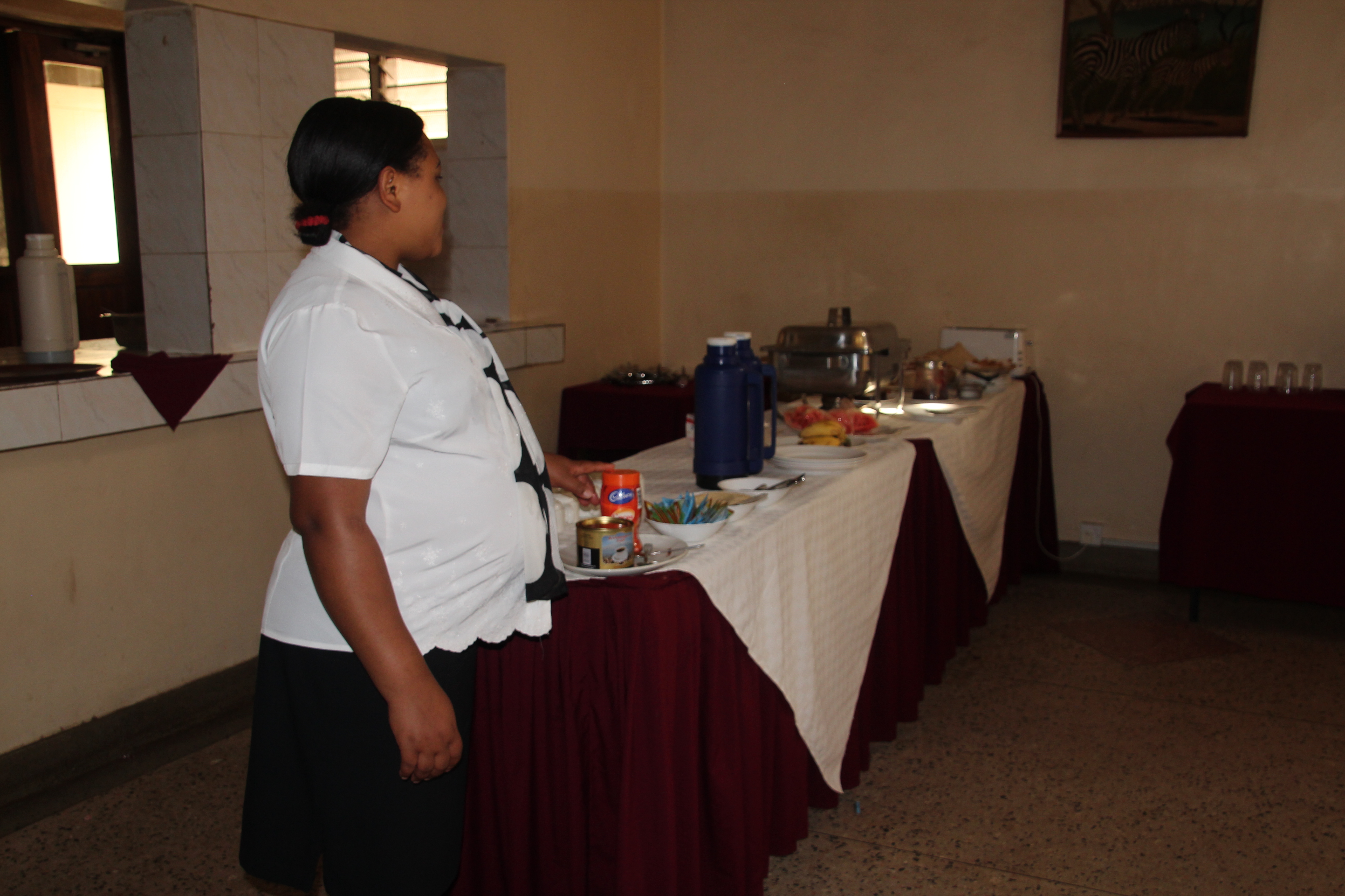 A pregnant woman working at a hotel, standing next to the breakfast buffet.