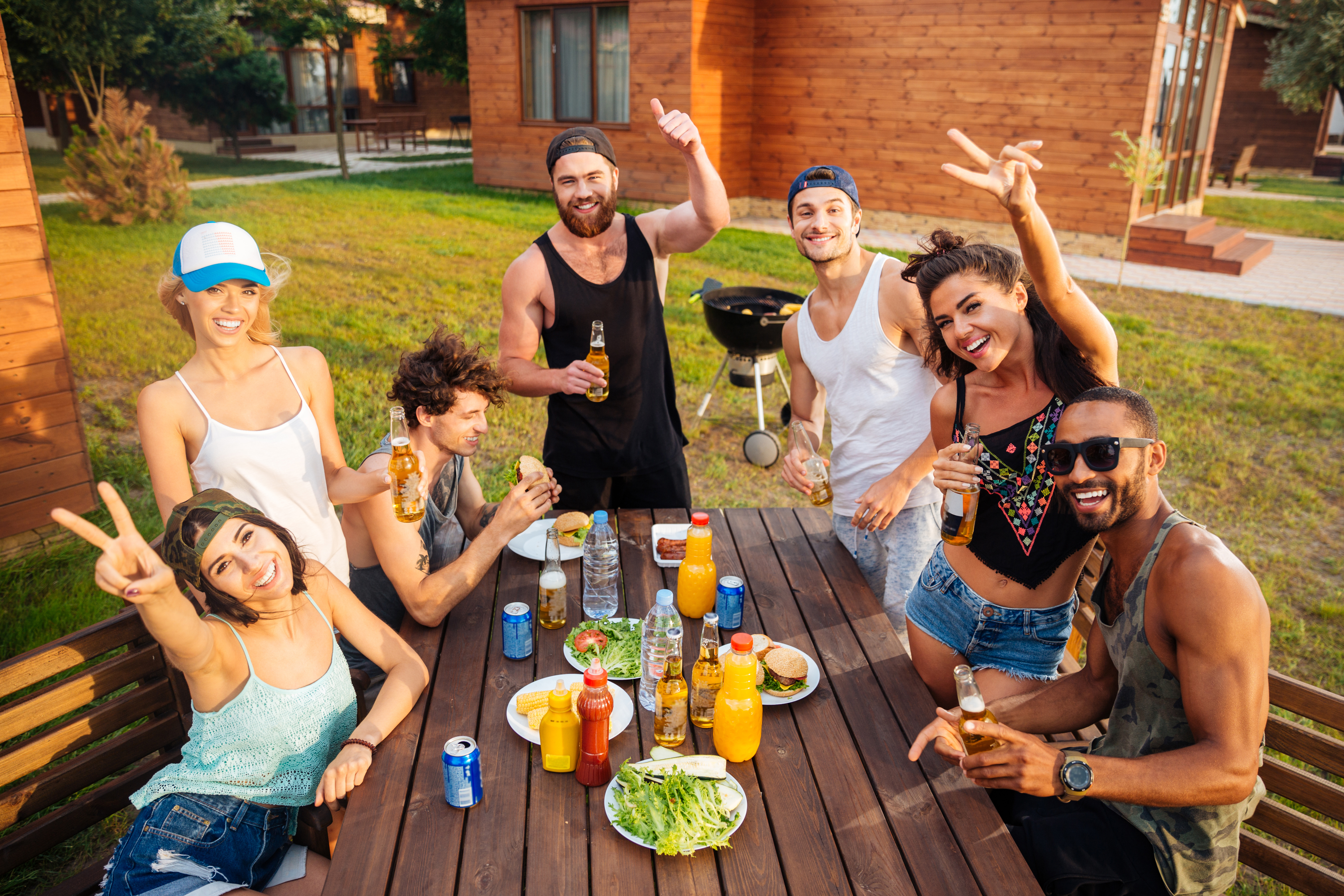 Group of cheerful young people having fun and eating at the table outdoors