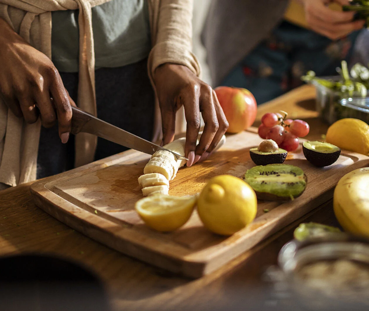 A person stood over a chopping board slicing various items of fruit