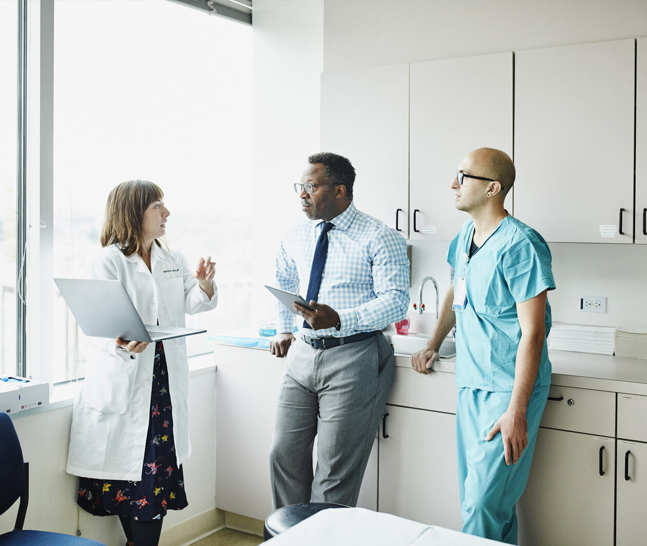 Female doctor leading medical team discussion in hospital exam room.