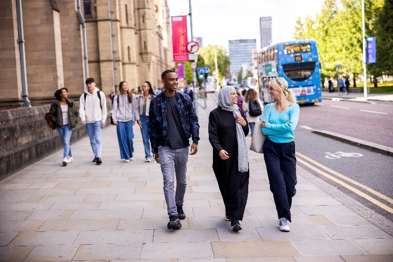 Three students walk on the pavement talking to each other