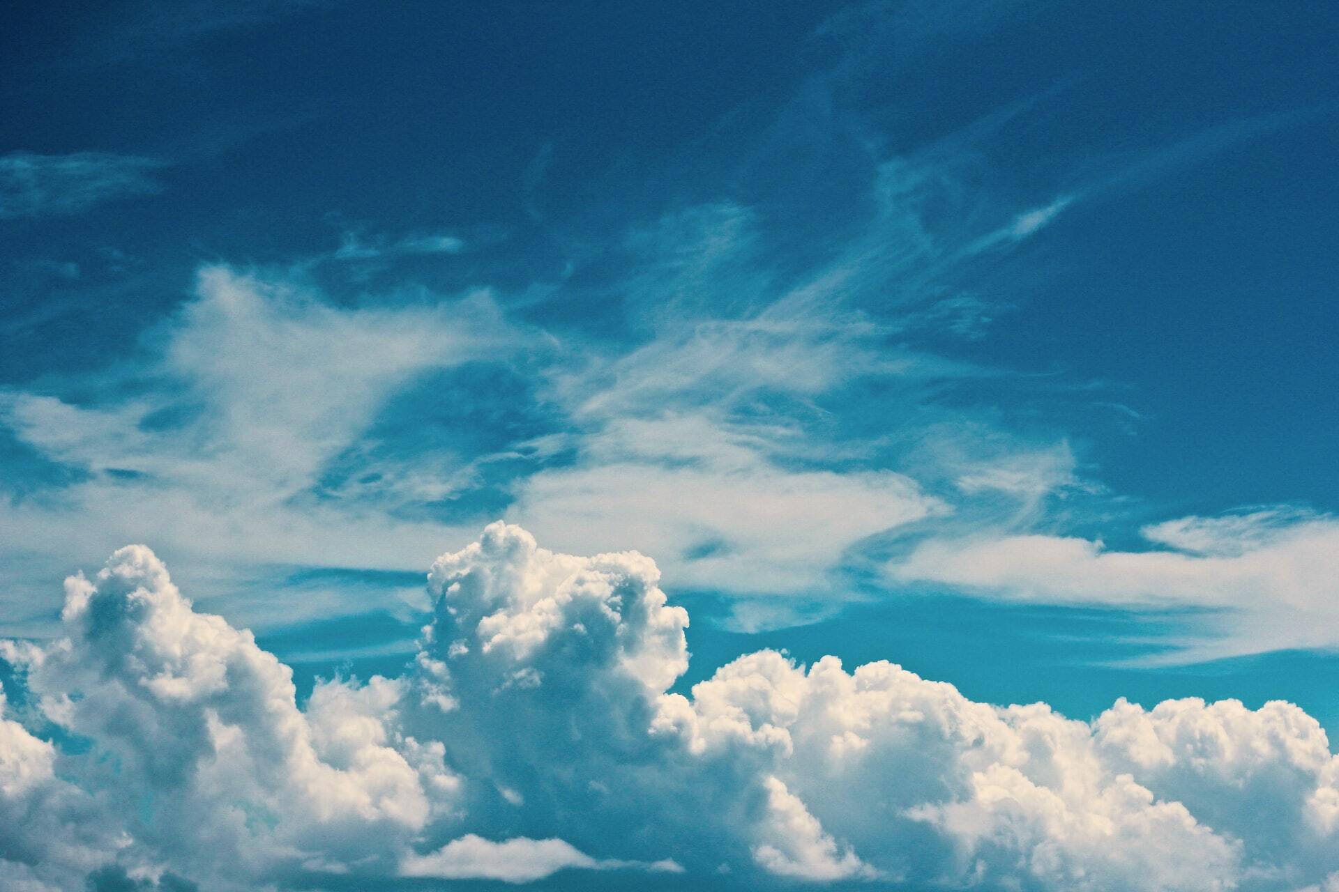 A deep blue sky, bordered by fluffy clouds and covered with wisps of other clouds, higher in the stratosphere.