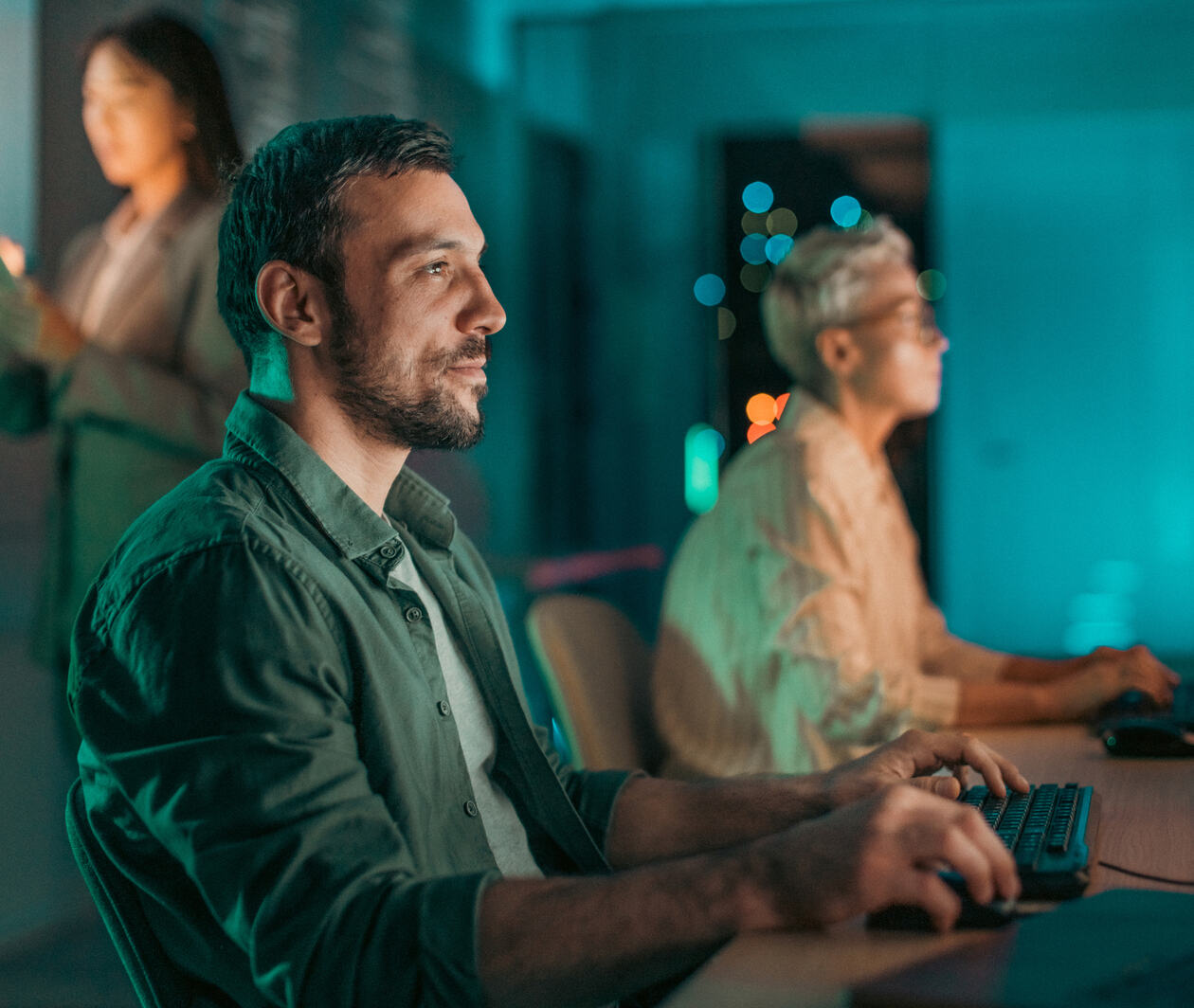 Confident young software engineer using a computer workstation during a night shift, working in a diverse team of tech professionals inside a data centre.