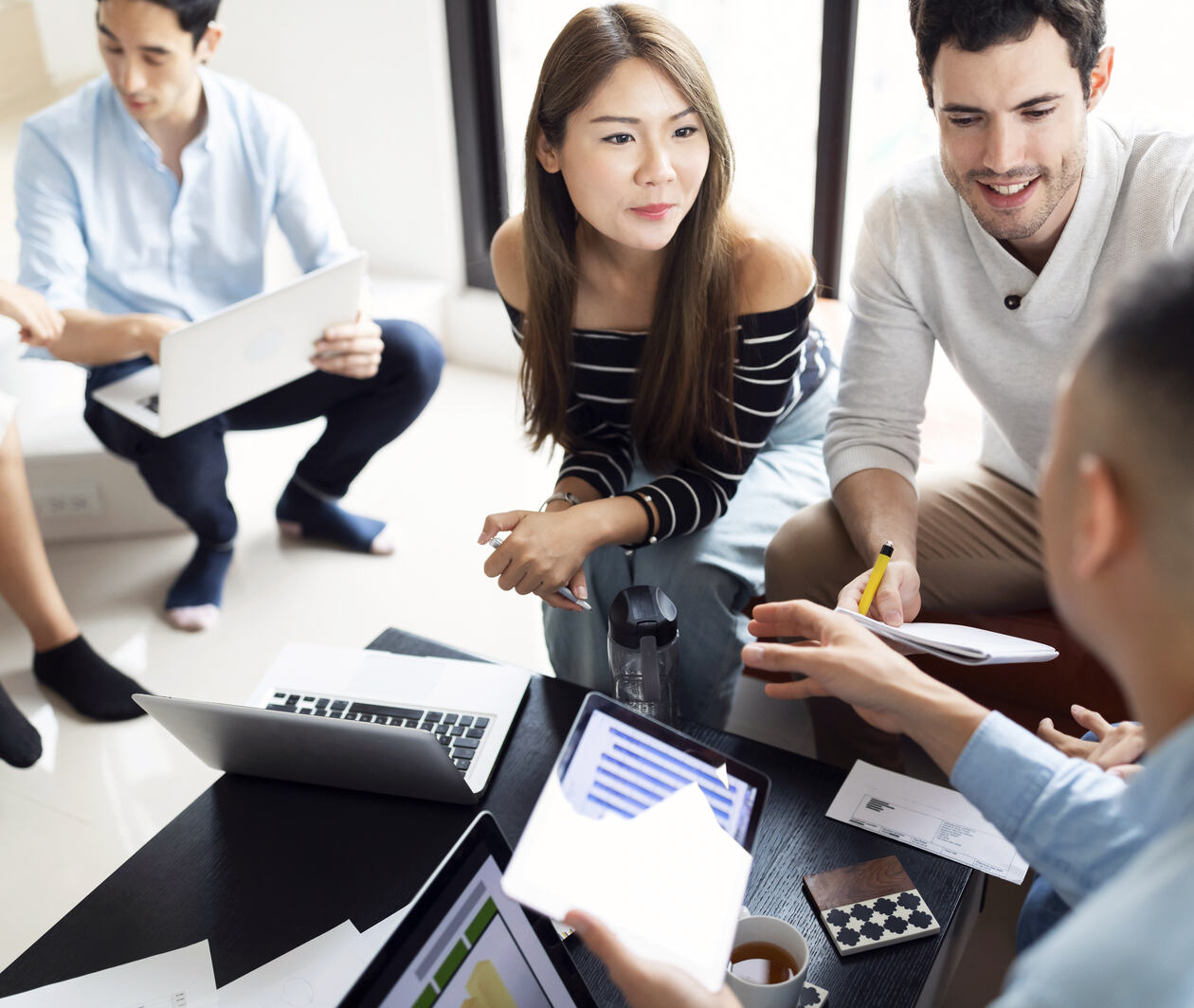 An asian woman speaking to a caucasian man surrounded by colleagues