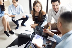 An asian woman speaking to a caucasian man surrounded by colleagues