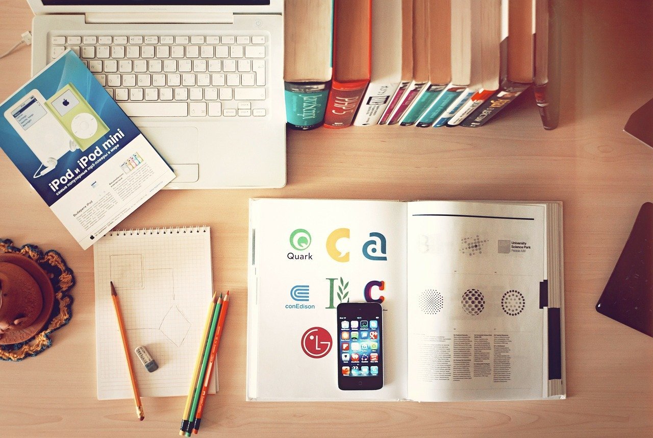 Looking down on a desk with a laptop, books, a calculator and some pens