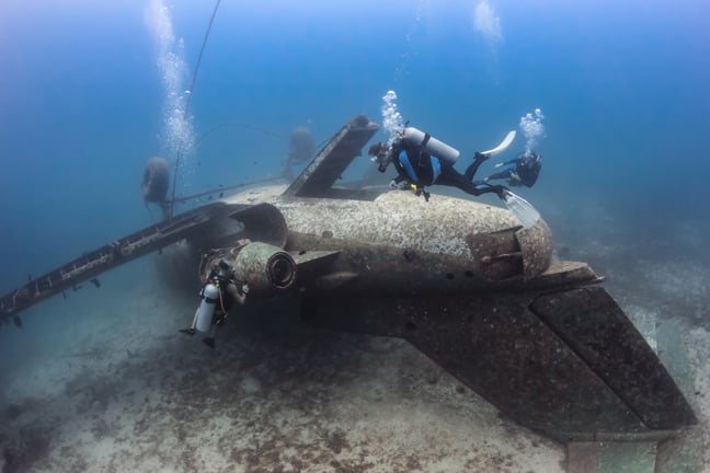 SCUBA divers exploring the upturned fuselage of an underwater aircraft wreck SCUBA divers exploring the upturned fuselage of an underwater aircraft wreck