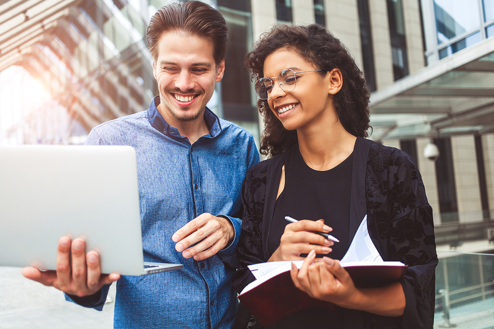 two people standing up in office, one holding a computer