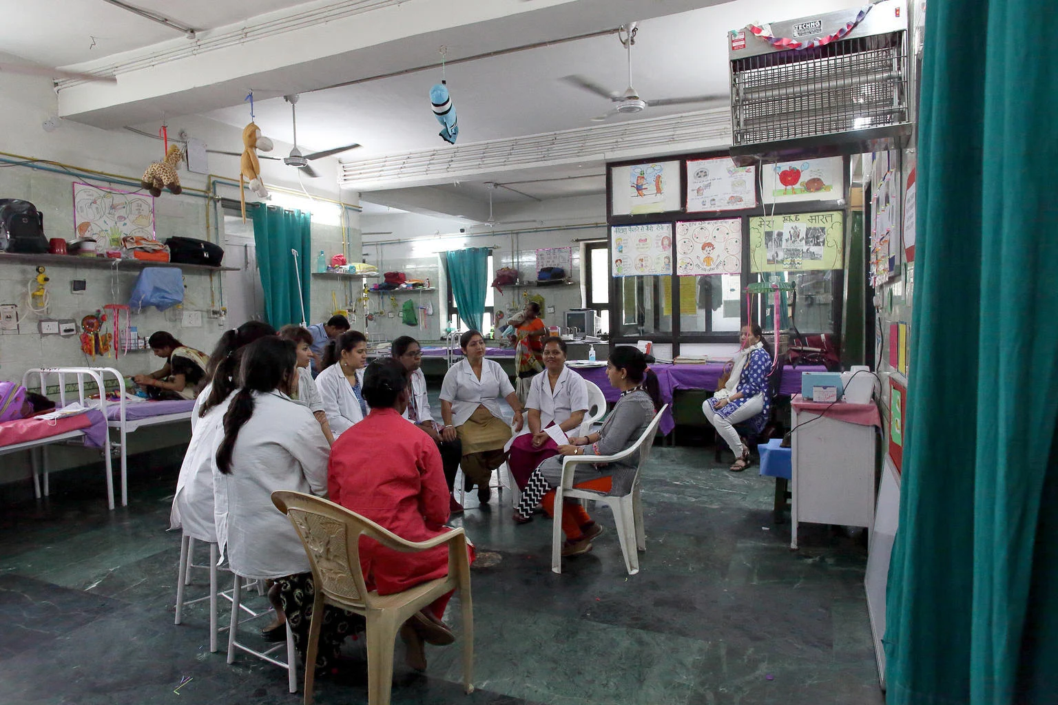 Hospital staff sit in a circle in the middle of a ward in a hospital in India for a staff meeting