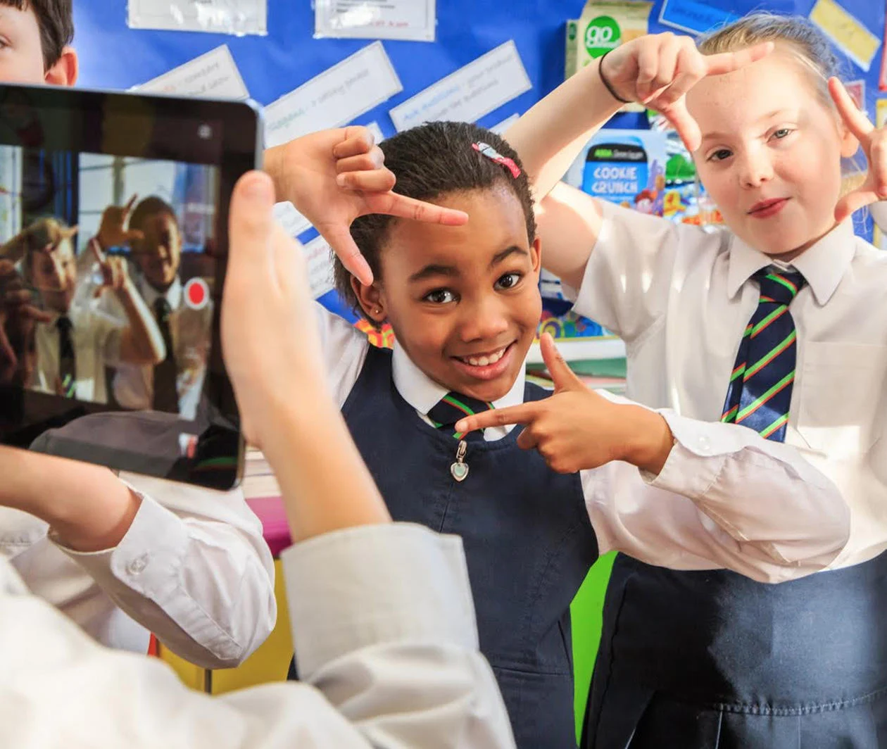 A child holds up an iPad to film other school children who are creating frames with their fingers..