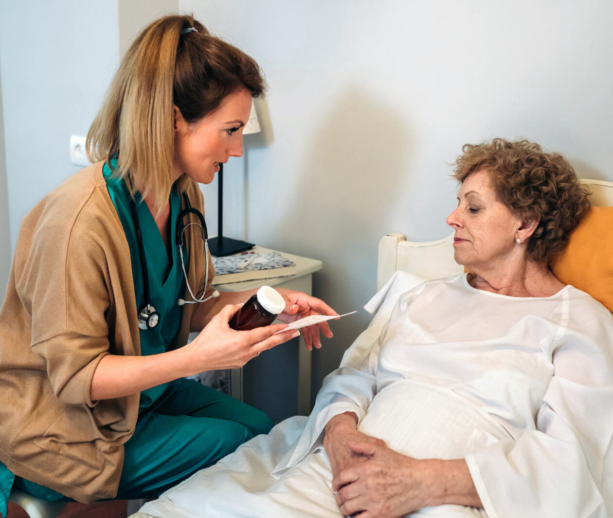 Patient sitting in front of a doctor and reading the label on a bottle of pills in his hand.