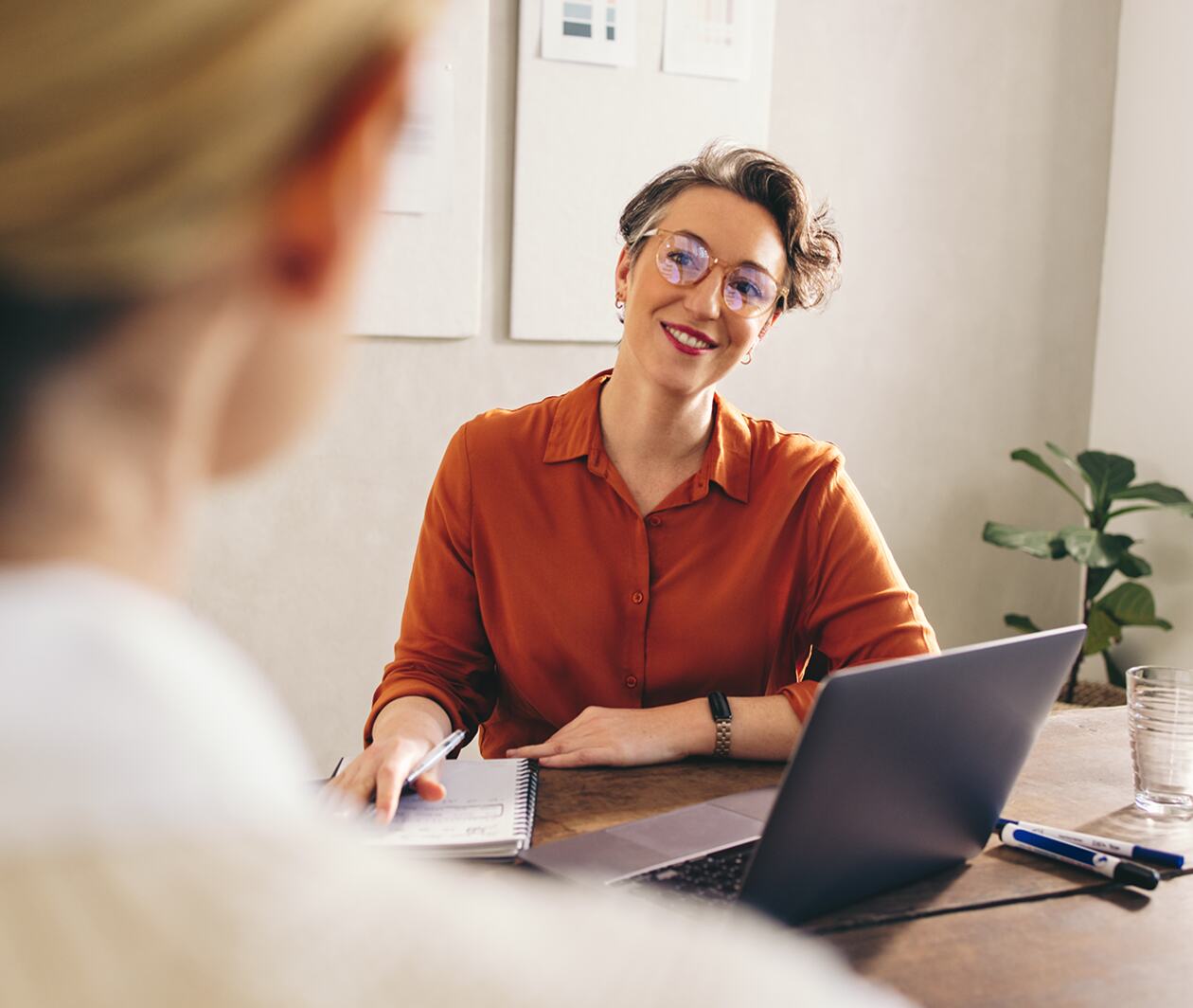 Professional woman sittnig at desk talking to a colleage