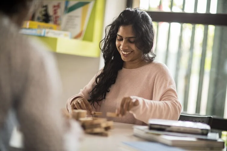 Secondary student sitting at table smiling and building with small wooden blocks