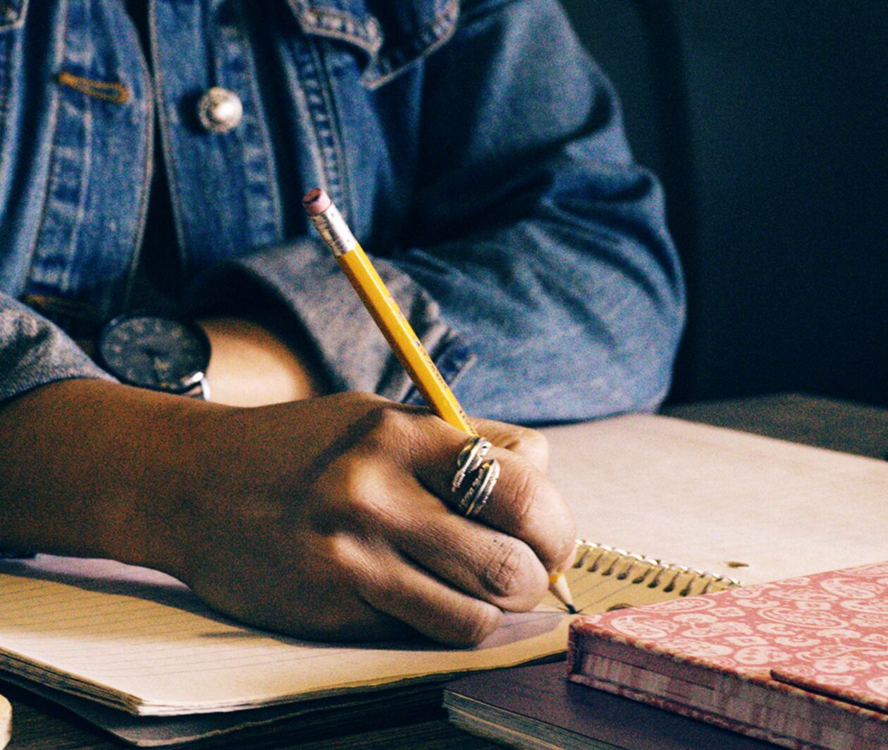 The hands of a person in a blue shirt writing in a notepad. 