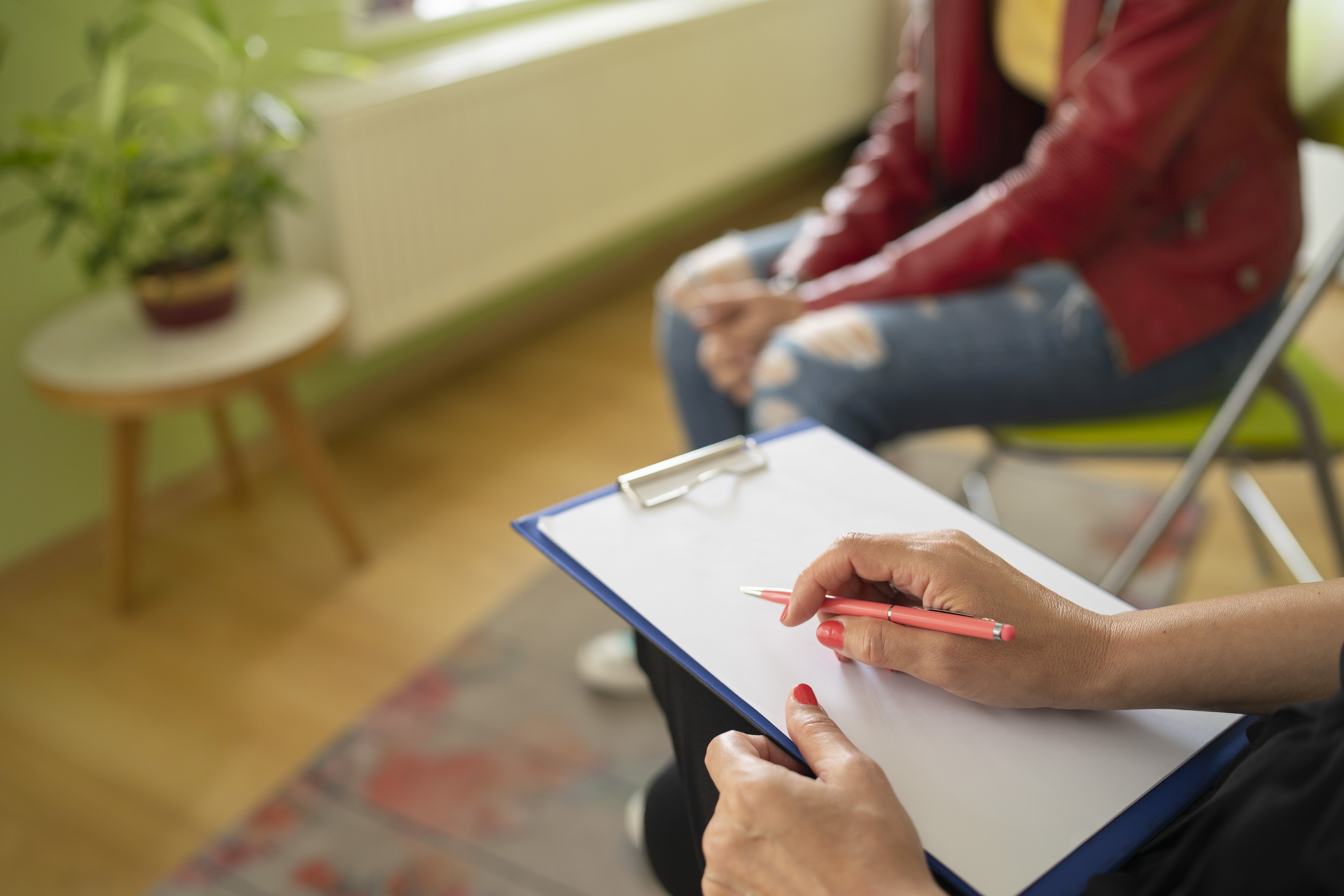 Close up of a psychologist notes and a students knees during a mental health meeting in a stylish office.