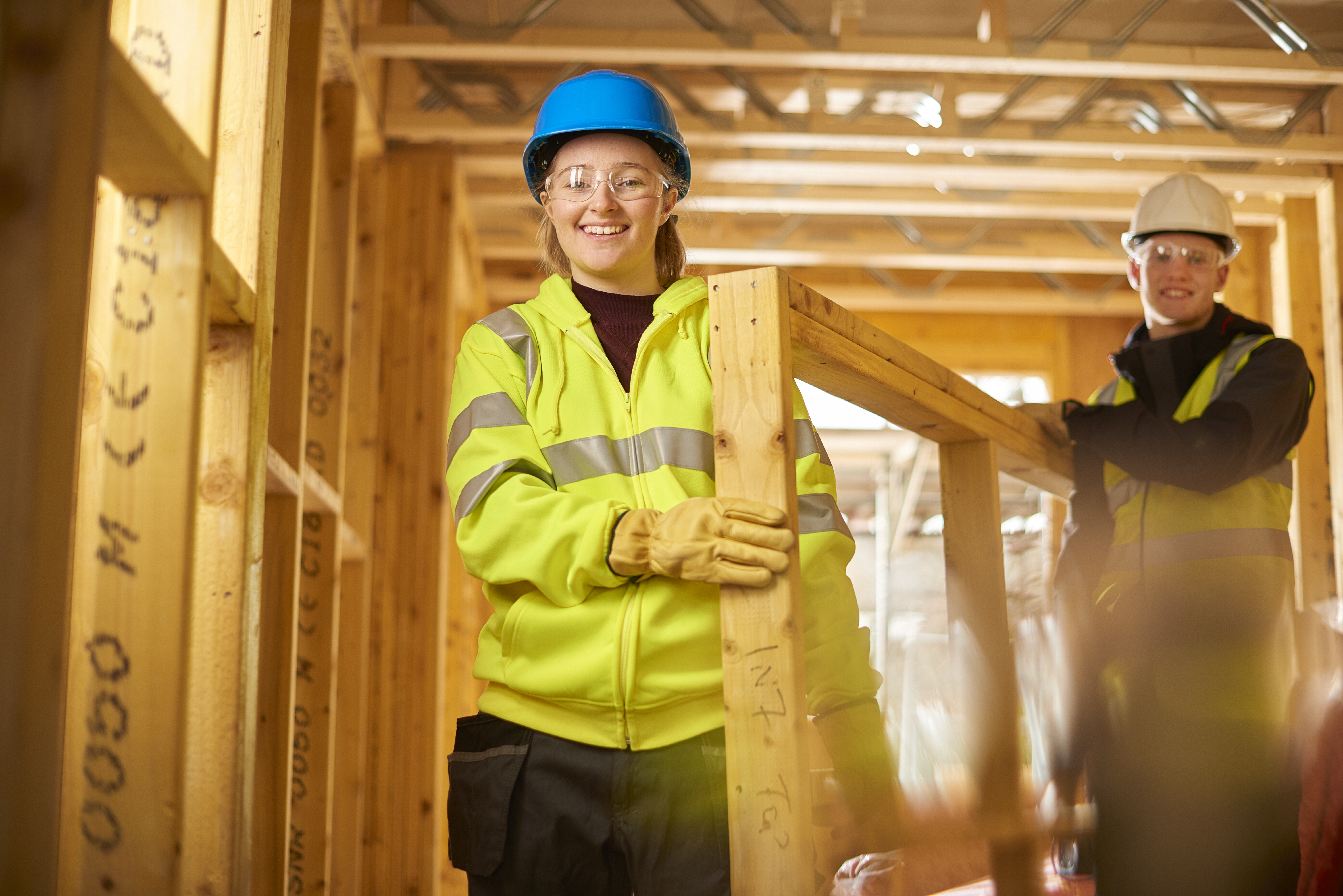 a female construction worker carries some studwork on a building site housing development and is assisted by a male colleague