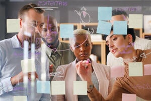 A group of colleagues gather around a post-it note board.