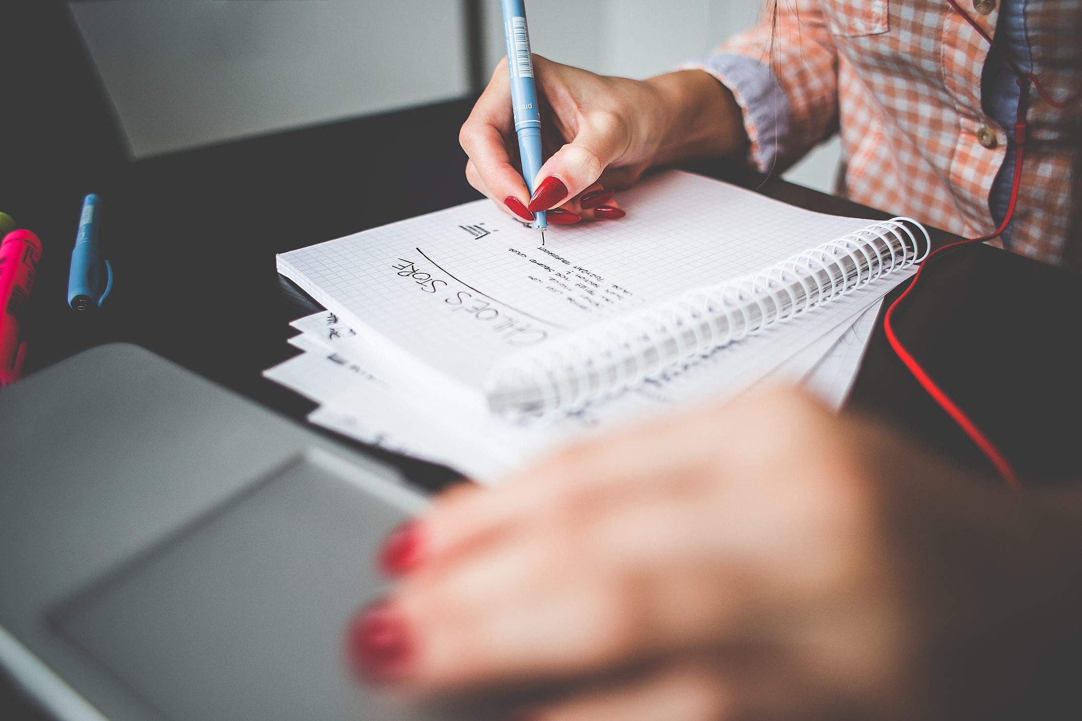 Person writing in a notepad with one hand hovering over a mousepad on a laptio