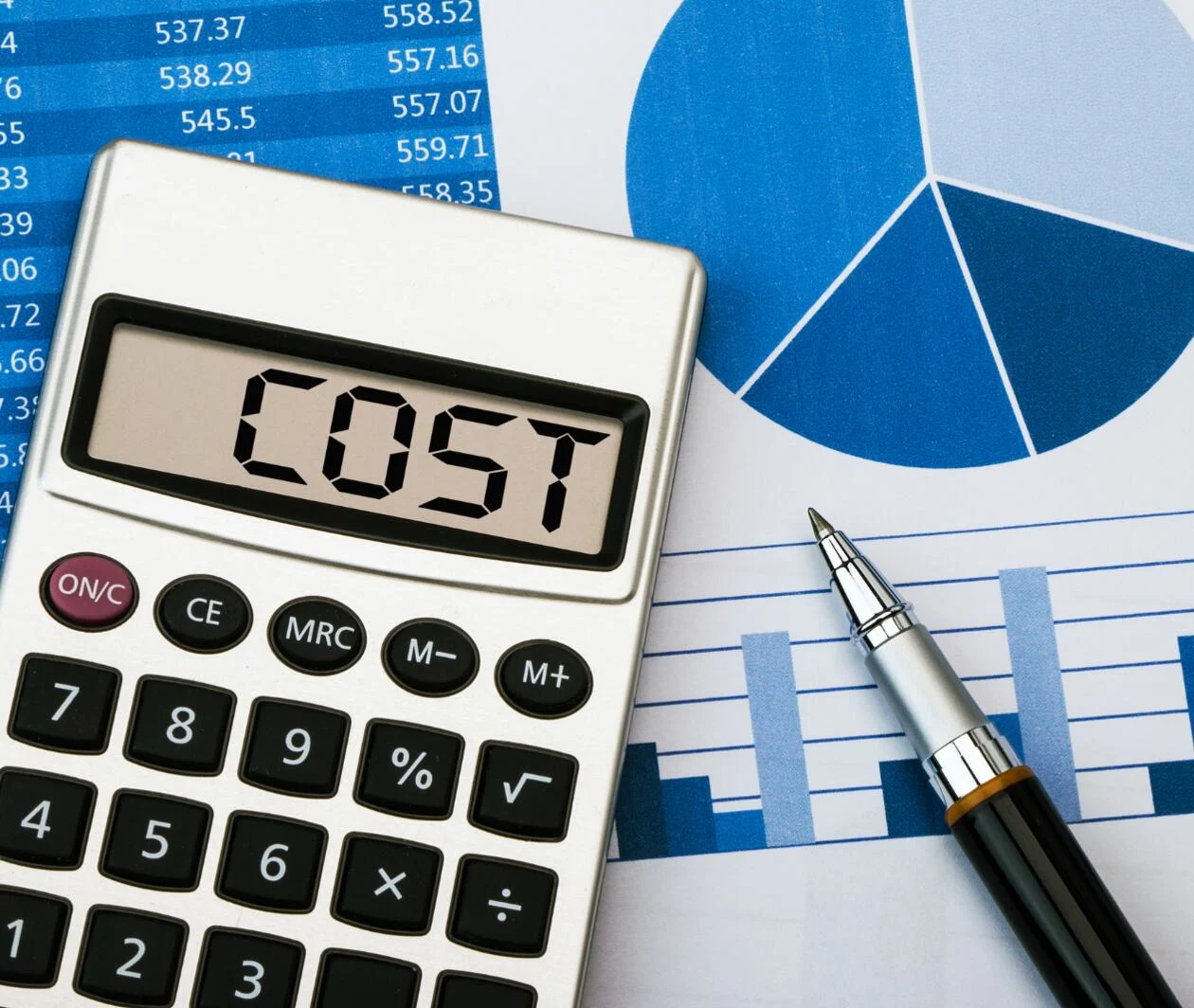 A calculator that reads 'Cost' with a pen next to it over a document displaying a blue pie chart, a table and a graph.